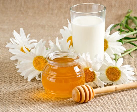Bowl with honey, glass with milk and daisies on the table